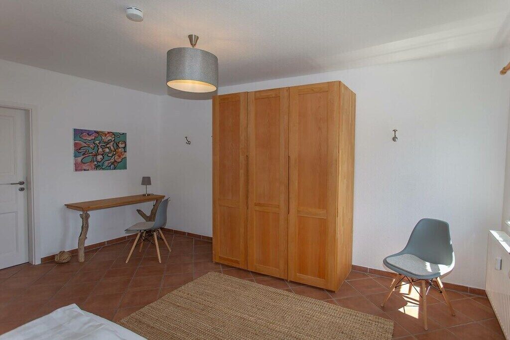 A room with a wooden wardrobe, a desk, a chair, a hanging light fixture, and a rug on the floor.