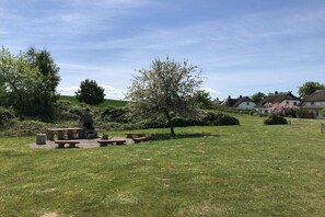 A grassy outdoor area with picnic tables and a stone structure, surrounded by houses and trees. - favorite spot in the thatched house (Putbus OT Wreechen)