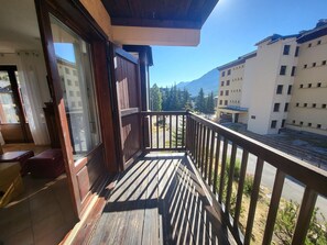 A balcony with a wooden railing overlooking a street and buildings, with a clear sky and mountains in the background. - Central apartment, balcony, south/east view (Montgenèvre)