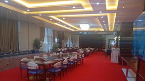 Un salón de conferencias con mesas y sillas dispuestas en filas, alfombra roja y un diseño moderno en el techo.