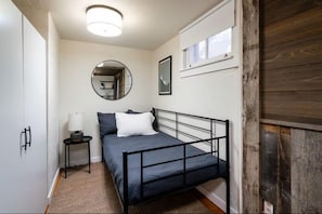 A bedroom with a bed, a bedside table, a mirror, and a window. - Downtown Bungalow- Modern Bungalow in the heart of Downtown Bozeman (Bozeman)