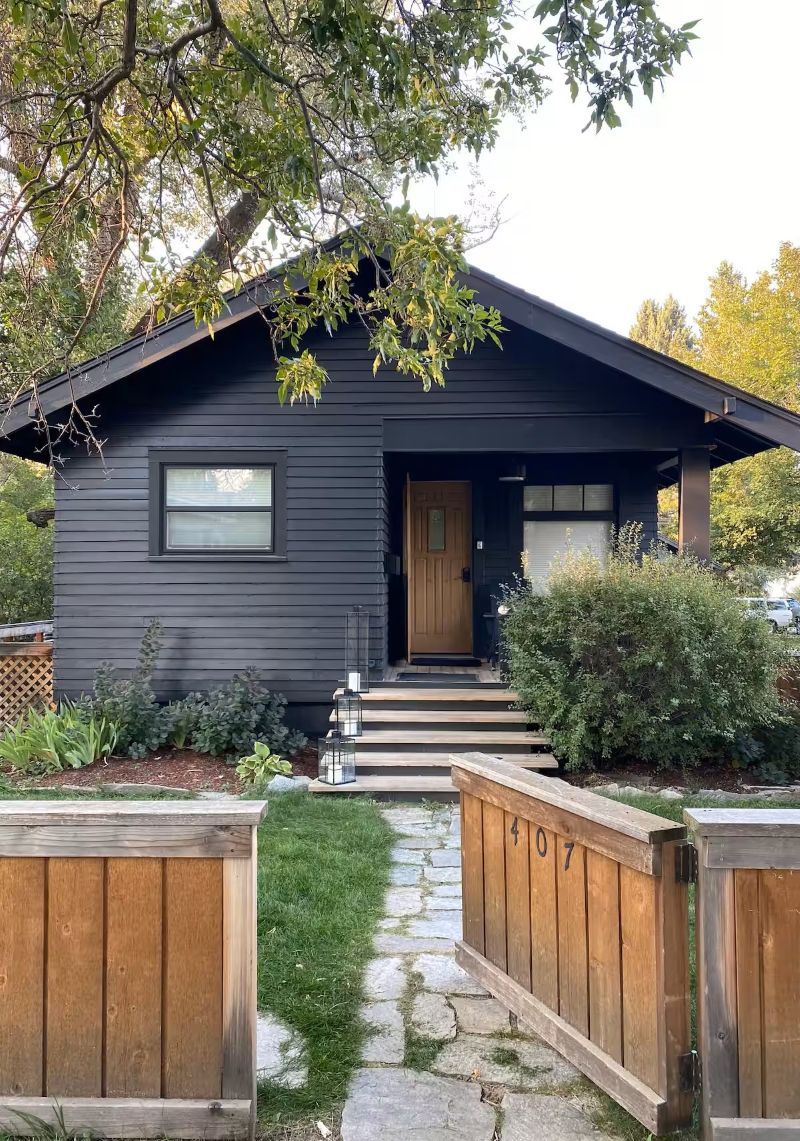 A dark-colored single-story house with a front door, a small porch, and a stone pathway leading to the entrance.