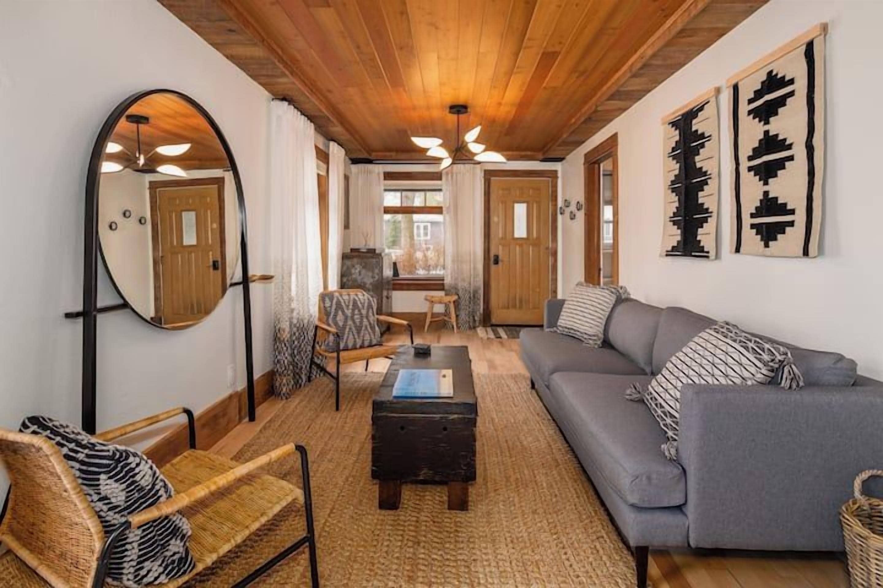 A cozy living room with a sofa, armchair, and a coffee table. There is a mirror on the wall and a door leading to another room.
