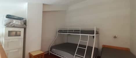 A small, single-bedded room with a bunk bed, a wooden desk, and a small stool.