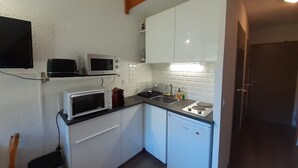 Eine kleine Küchenzeile mit weißen Schränken, einer Mikrowelle, einem Toaster und einem Spülbecken.