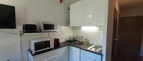 A compact kitchenette with white cabinets, a microwave, a toaster, and a sink.