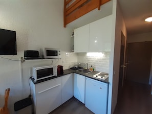 Een kleine keuken met witte kastjes, een magnetron, een broodrooster en een spoelbak.
