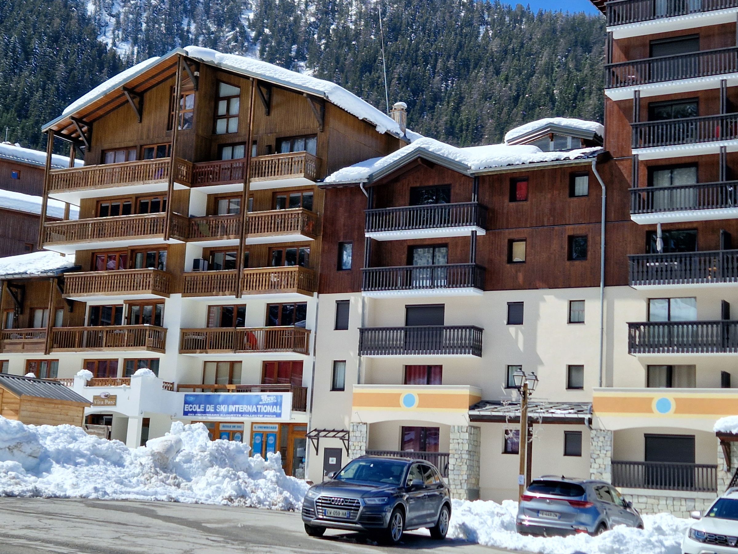 A multi-story hotel with wooden balconies and snow-covered roofs, located in a mountainous area.