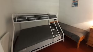 Ein Stockbett mit einer Leiter, ein Einzelbett, eine Kommode und ein an der Wand befestigtes Bild.