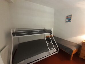 Een stapelbed met een ladder, een enkel bed, een dressoir en een aan de muur hangend schilderij.