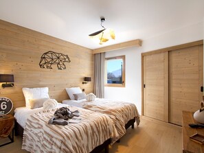 A hotel room with a wooden wall, a bed with a patterned blanket, a geometric wall decoration, and a window with a mountain view. - Bright apartment with pool - ski-in/ski-out (Huez)