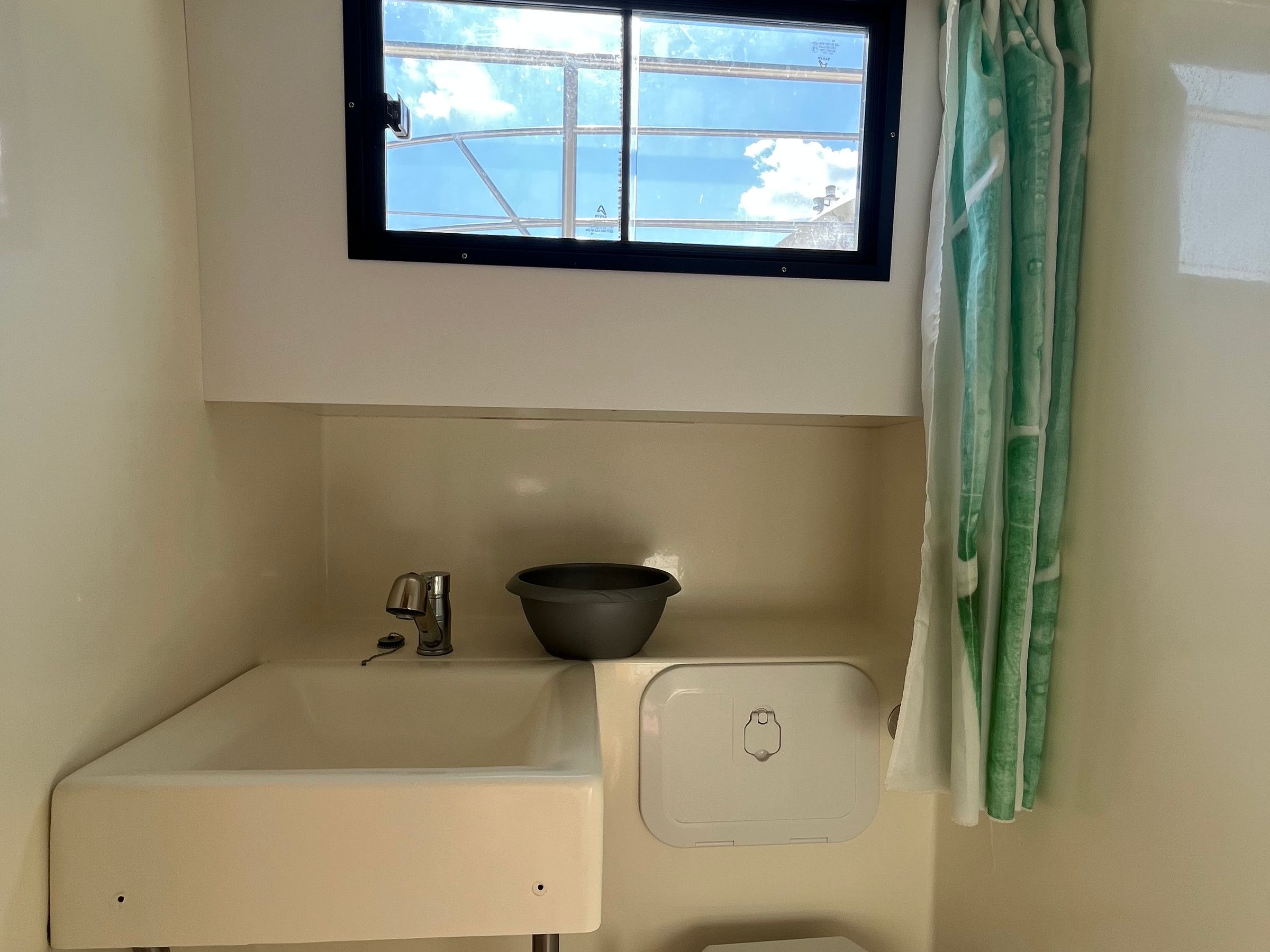 Een compacte badkamer met een raam, een wastafel en een douchegordijn.