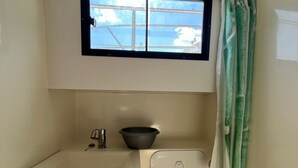 Een compacte badkamer met een raam, een wastafel en een douchegordijn.