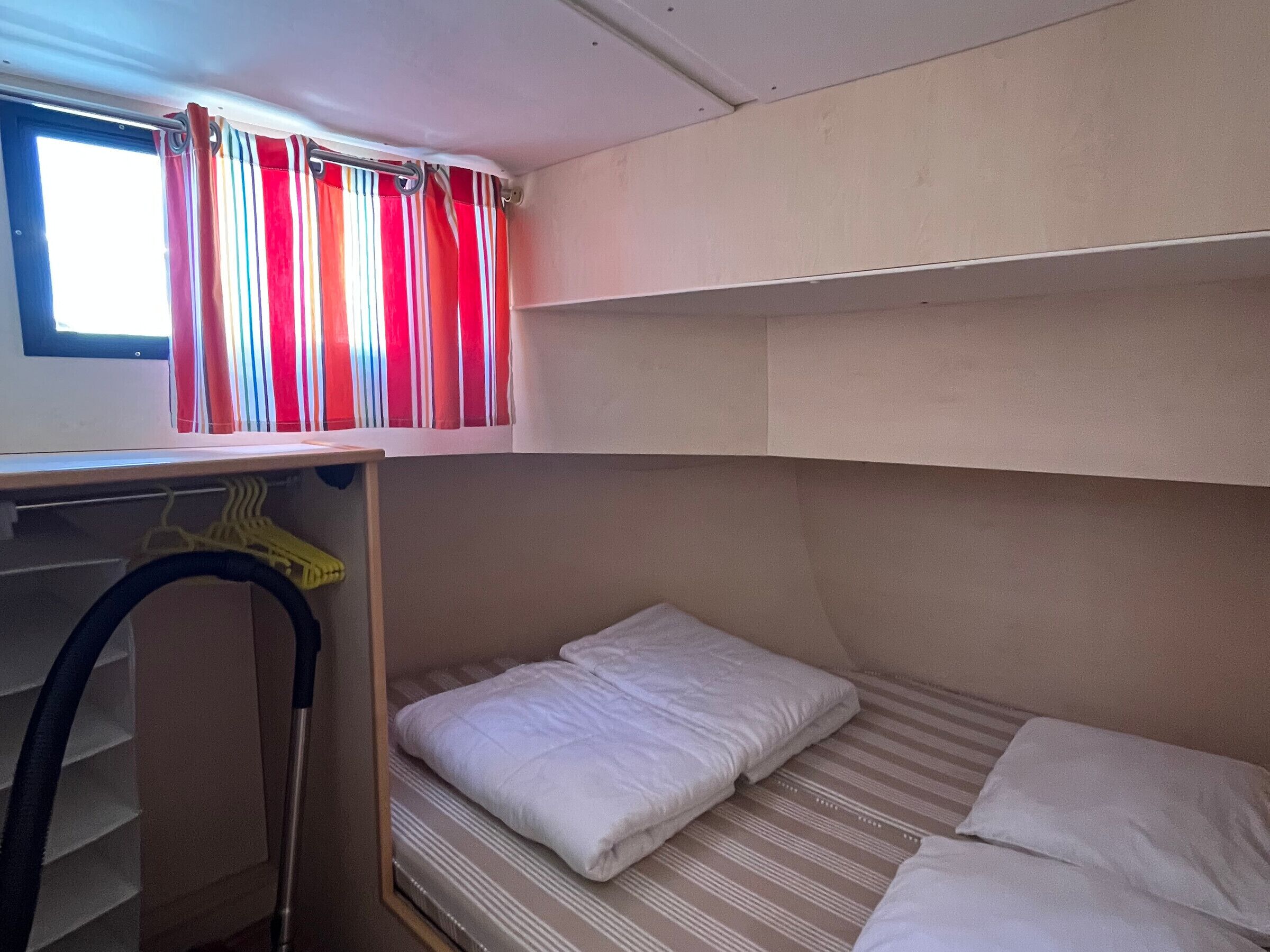 Een stapelbed met een raam erboven, een plank met een gele ophanger en een kast met een kledingroede.