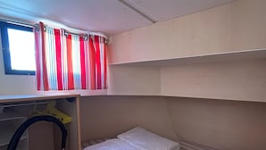 Een stapelbed met een raam erboven, een plank met een gele ophanger en een kast met een kledingroede.