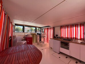 A compact kitchen with a dining area, a red table, and a view through the windows. - Unique houseboat in Digoin - 12 guests (Digoin)