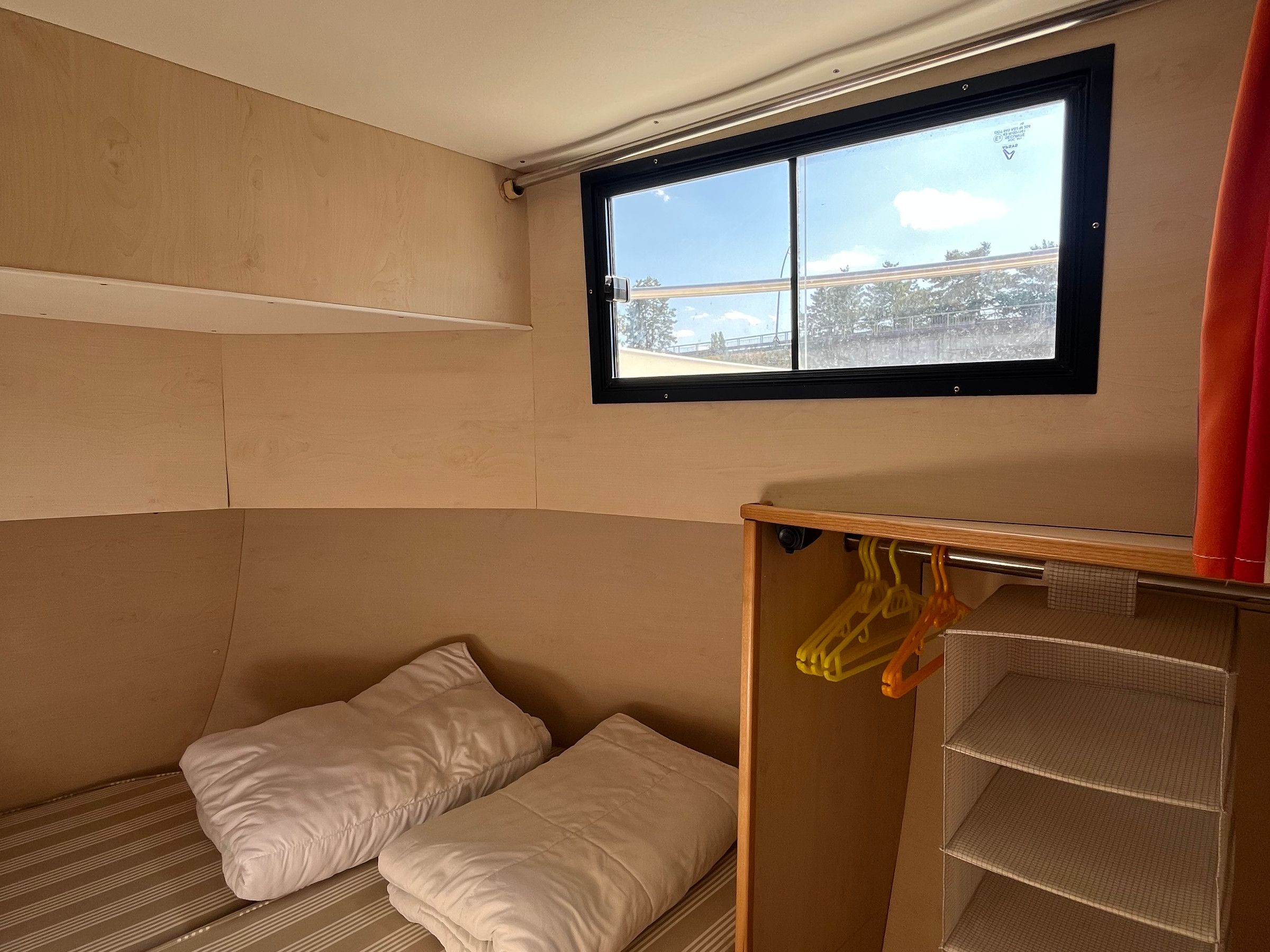 Una stanza con un letto a castello, una finestra vista e un armadio con grucce.