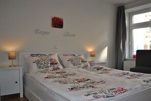 A bedroom with a bed, two bedside lamps, a window with curtains, and a wall with a red rose decoration. - Holiday apartment in Leipzig with Wi-Fi (Leipzig)