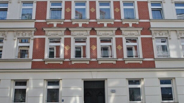 En fleretagers bygning med en symmetrisk facade, central indgang med en sort dør, og jævnt fordelte vinduer på hver etage.