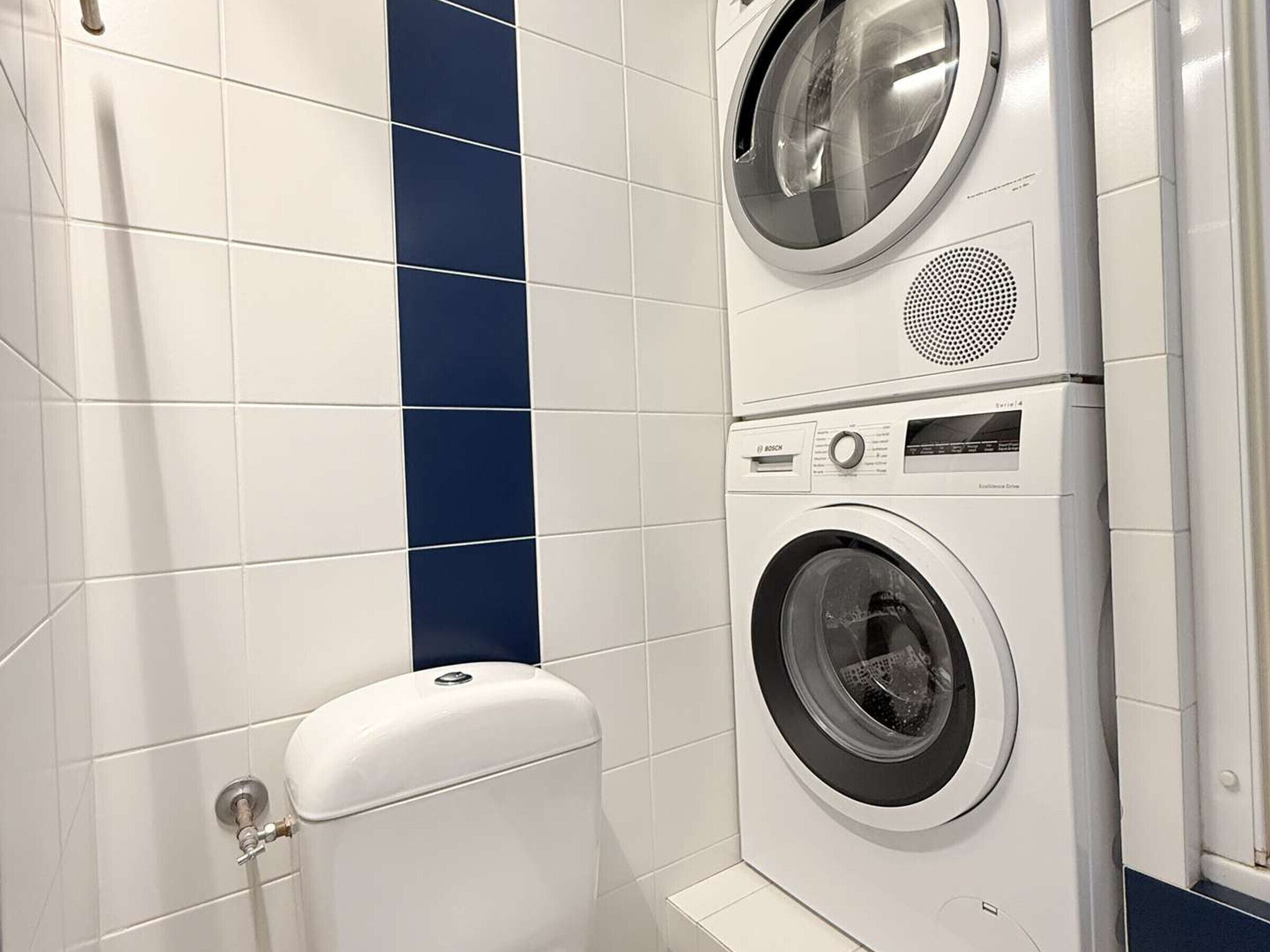 A compact laundry room with a Bosch washing machine and dryer, a toilet, and a blue accent wall.