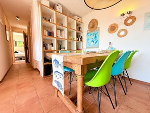 Un comedor con una mesa de madera, sillas verdes y una estantería llena de libros y botellas.