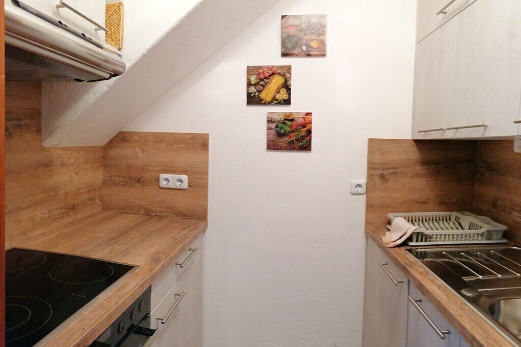 A compact kitchen with a wooden countertop, a stove, and a sink. There are three small framed pictures on the wall.