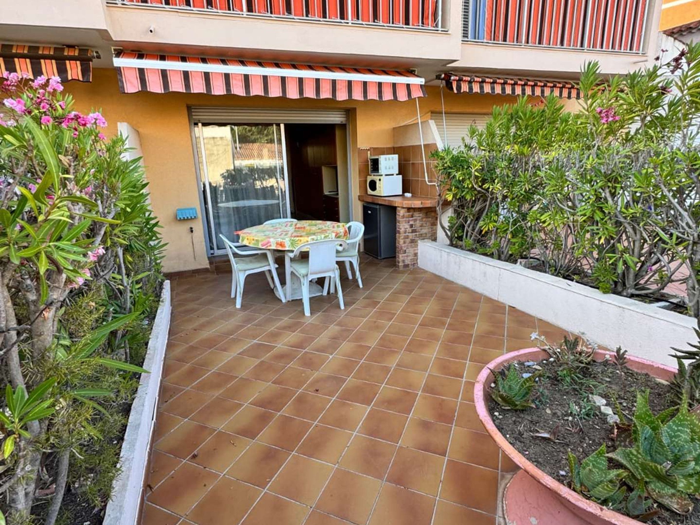 Eine Terrasse mit Fliesenboden, einem Tisch mit Stühlen und Topfpflanzen.