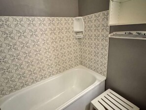 Et badeværelse med et hvidt badekar, mønstret flisearbejde og et håndklædestativ.