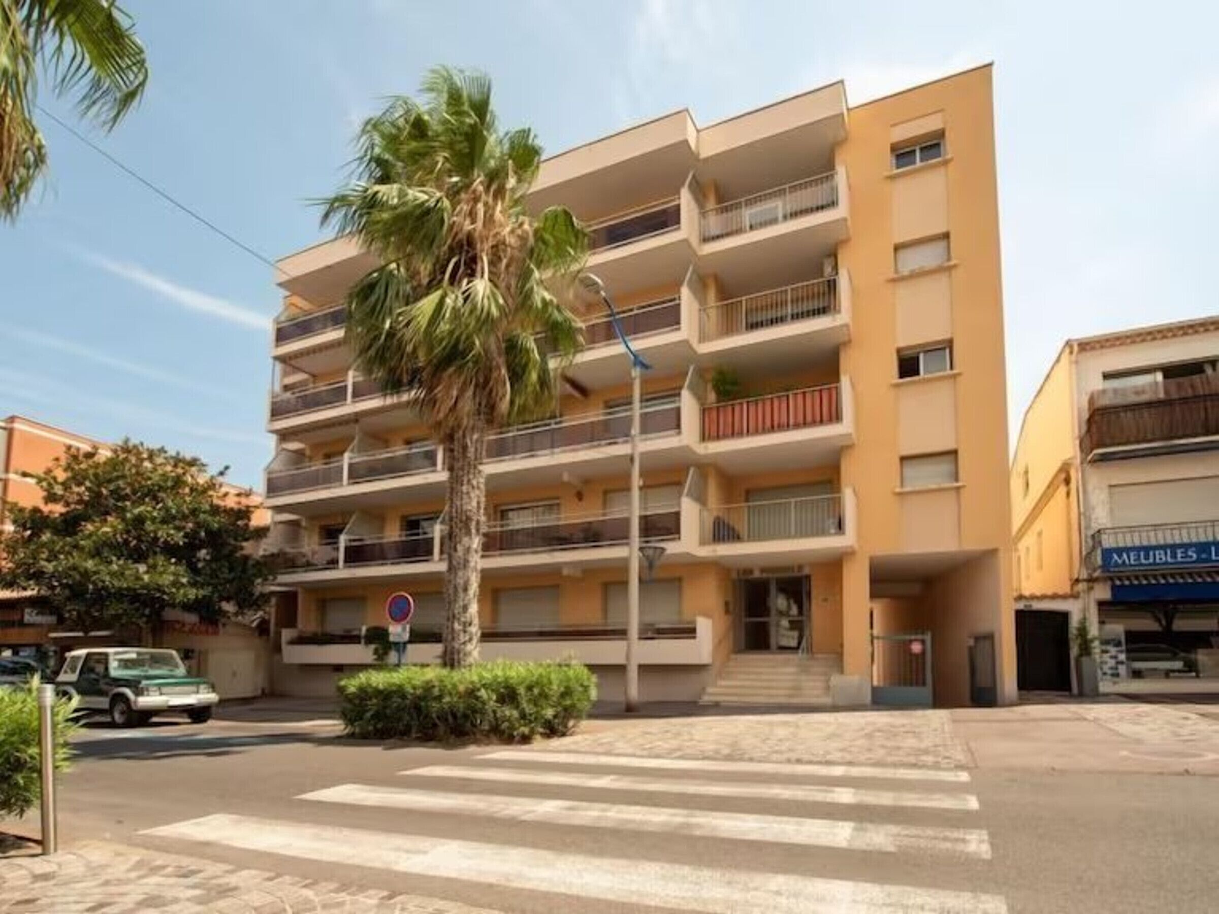 A multi-story building with balconies, a palm tree, and a crosswalk.