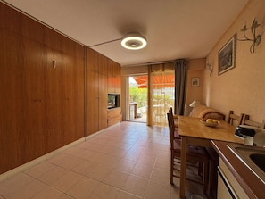 A kitchen with wooden cabinets, a dining table with chairs, a TV, and a ceiling light. - Studio with parking - 4 guests in Cavalaire (Cavalaire-sur-Mer)