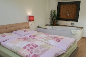 A bedroom with a bed, a red wall lamp, a wooden headboard, a white bathtub, and a wooden wall panel. - viaDolceVita - Green Guest Apartment (Lana)