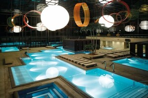 Ein Poolbereich mit mehreren Pools, Liegestühlen und einem modernen Deckenstil mit runden Leuchten.