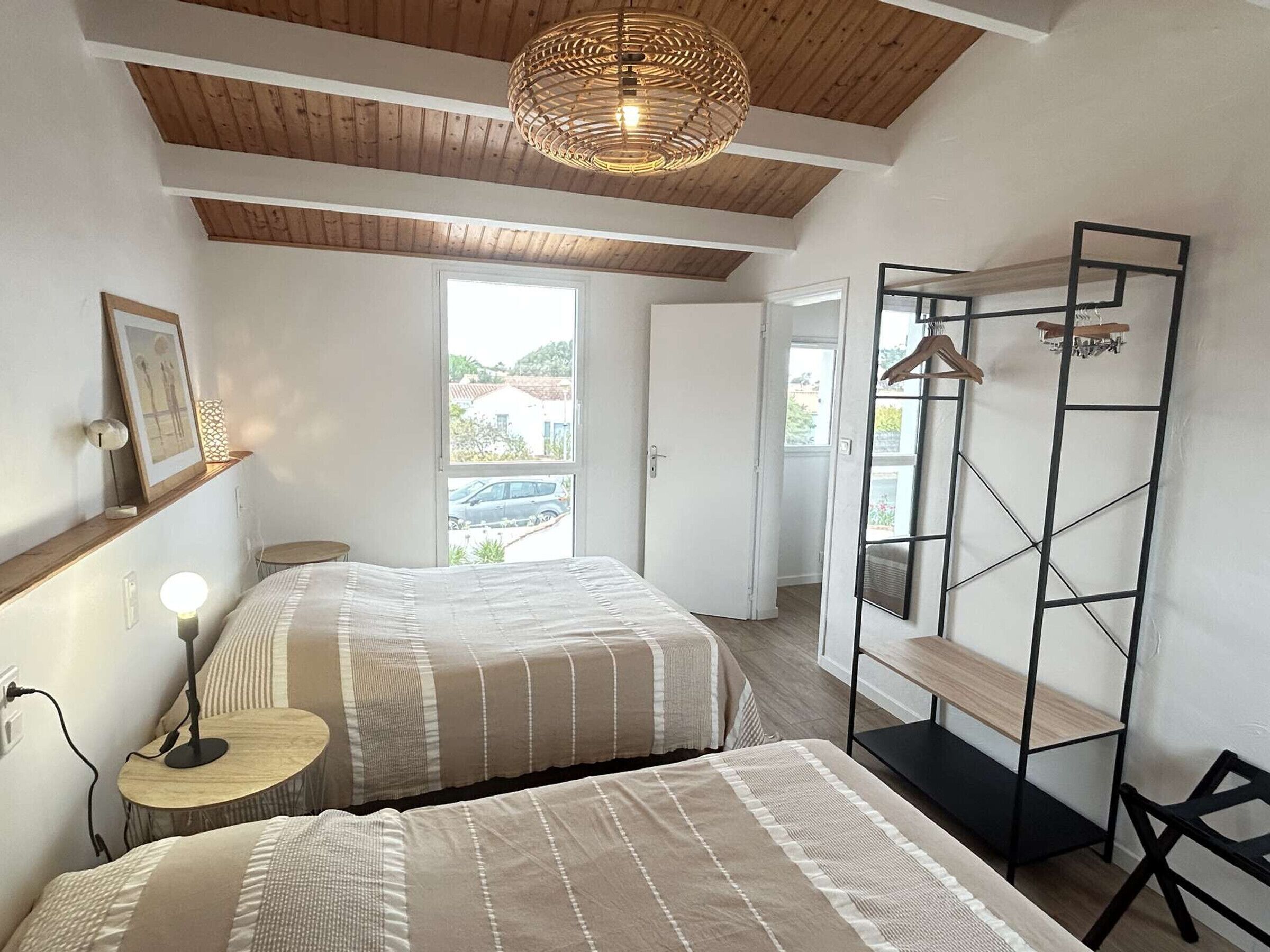 A bedroom with two beds, a hanging light fixture, a bedside table, and a wardrobe with a hanging rack.