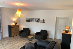 Een moderne woonkamer met twee zwarte fauteuils, een bank, een houten kast en een hanglamp.