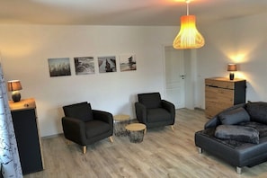 A modern living room with two black armchairs, a sofa, a wooden cabinet, and a hanging lamp. - Holiday apartment with 2 bedrooms (Dresden)