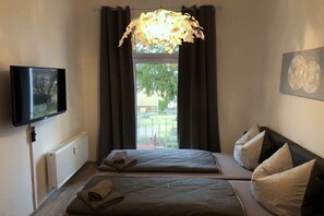 A hotel room with a bed, a flat-screen TV, a radiator, a window with curtains, and a painting on the wall. - Holiday apartment with 2 bedrooms (Dresden)