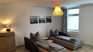 Une chambre moderne avec deux lits simples, une commode en bois, une lampe suspendue et une fenêtre avec des rideaux.