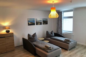 Ein modernes Schlafzimmer mit zwei Einzelbetten, einer Holzkommode, einer Hängelampe und einem Fenster mit Vorhängen.
