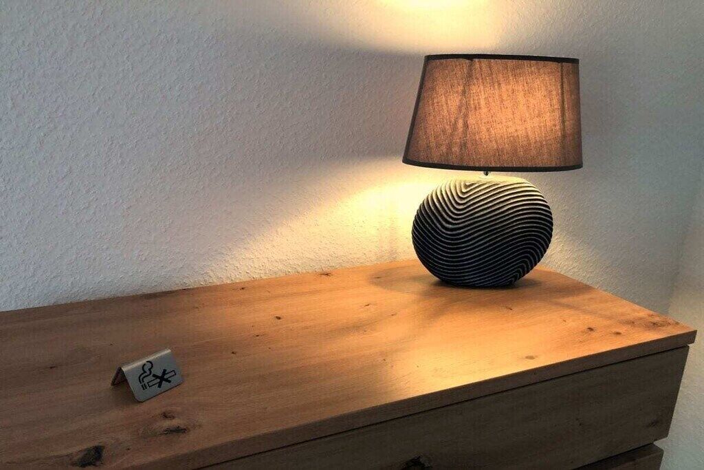 A wooden bedside table with a lamp and a small object on it.