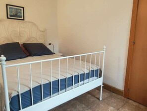 A single bed with a white metal frame, a headboard with a decorative design, and a wooden door to the right. - Apartment with parking in city center - 3 guests (Amélie-les-Bains-Palalda)
