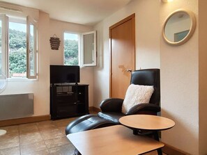A room with a television, a black leather chair with a white pillow, a small round table, and a wooden door. - Apartment with parking in city center - 3 guests (Amélie-les-Bains-Palalda)