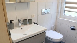 Et badeværelse med en hvid vask, toilet og et vindue med persienner.