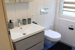 Un bagno con un lavandino bianco, un water e una finestra con persiane.