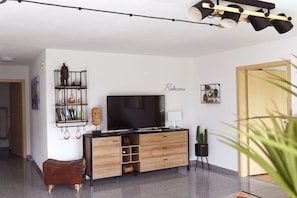 Ein modernes Wohnzimmer mit Flachbildfernseher, Holzmöbeln, einer Regal mit Dekoration und einer Pflanze.