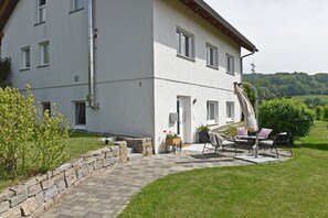 Un edificio a due piani con patio lastricato, posti a sedere all'aperto e un muro in pietra.