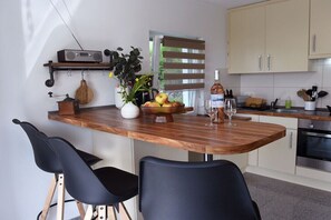 A modern kitchen with a wooden island, black chairs, a radio, and a fruit bowl. - Holiday apartment with 1 bedroom (Frickingen)