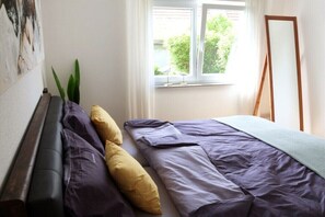 Una camera da letto con un letto, una finestra con tende, uno specchio a figura intera e un quadro appeso al muro.