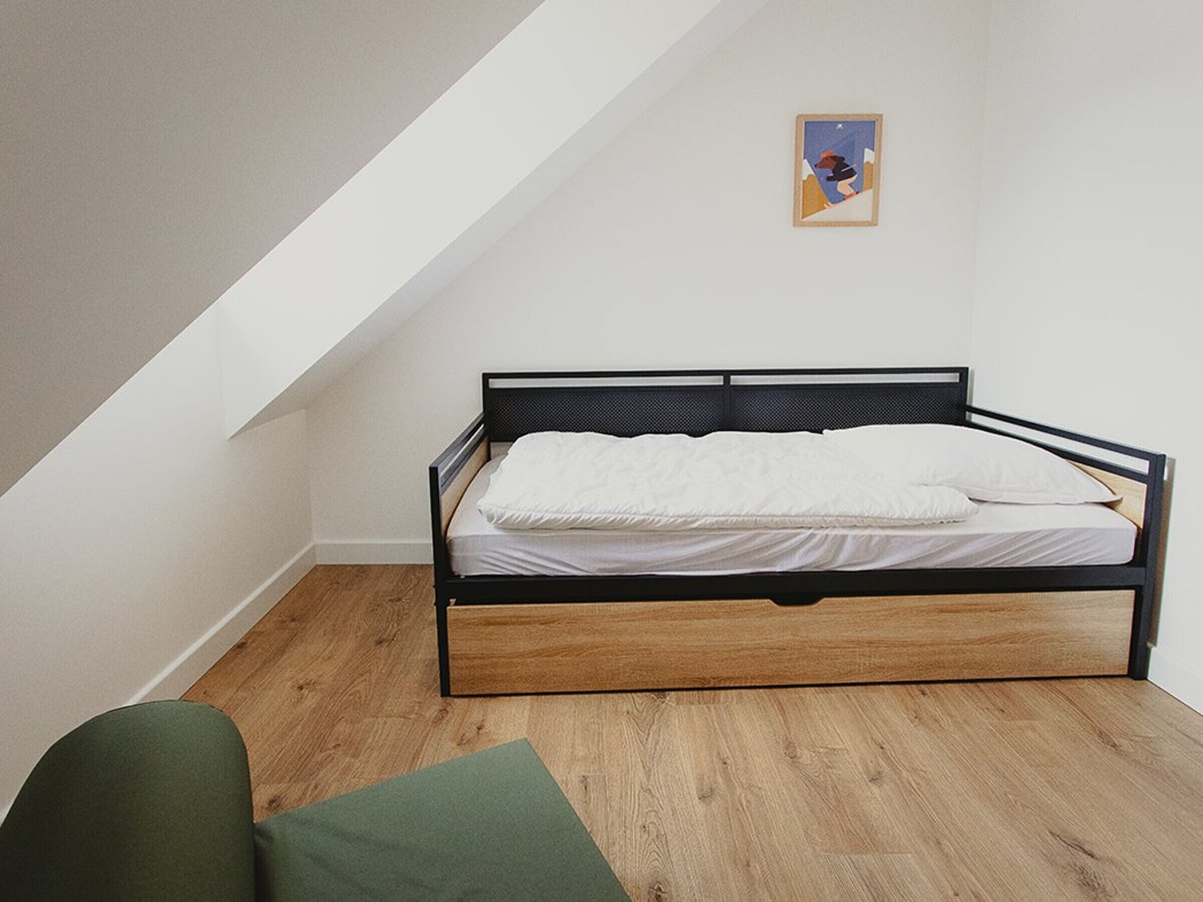 Een enkel bed met houten frame en matras in een kamer met schuine plafonds.