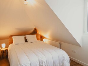 A bedroom with a sloped ceiling, a bed with white bedding, a nightstand with a lamp, and a window on the right. - Duplex apartment with parking - 5 guests (Saint-Lary-Soulan)