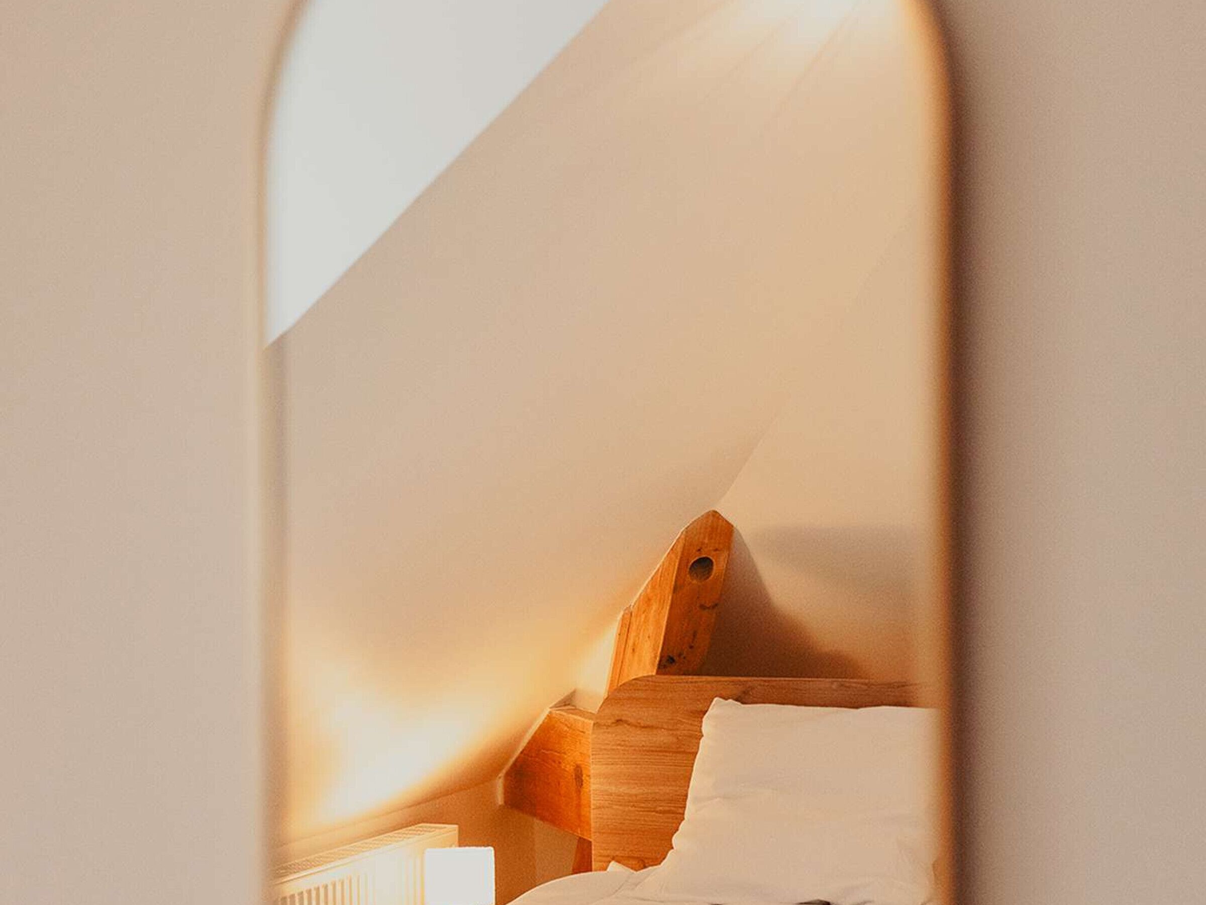 Una habitación pequeña con techo inclinado, una litera de madera y un radiador blanco.